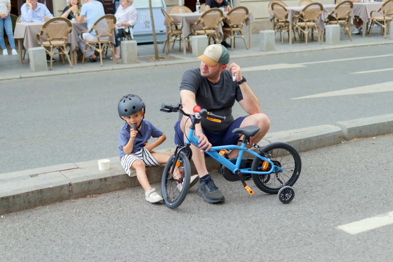 8 - Father and child relaxing near a bright blue B'Twin Discover 500 kids' bike featuring training wheels and orange reflectors
